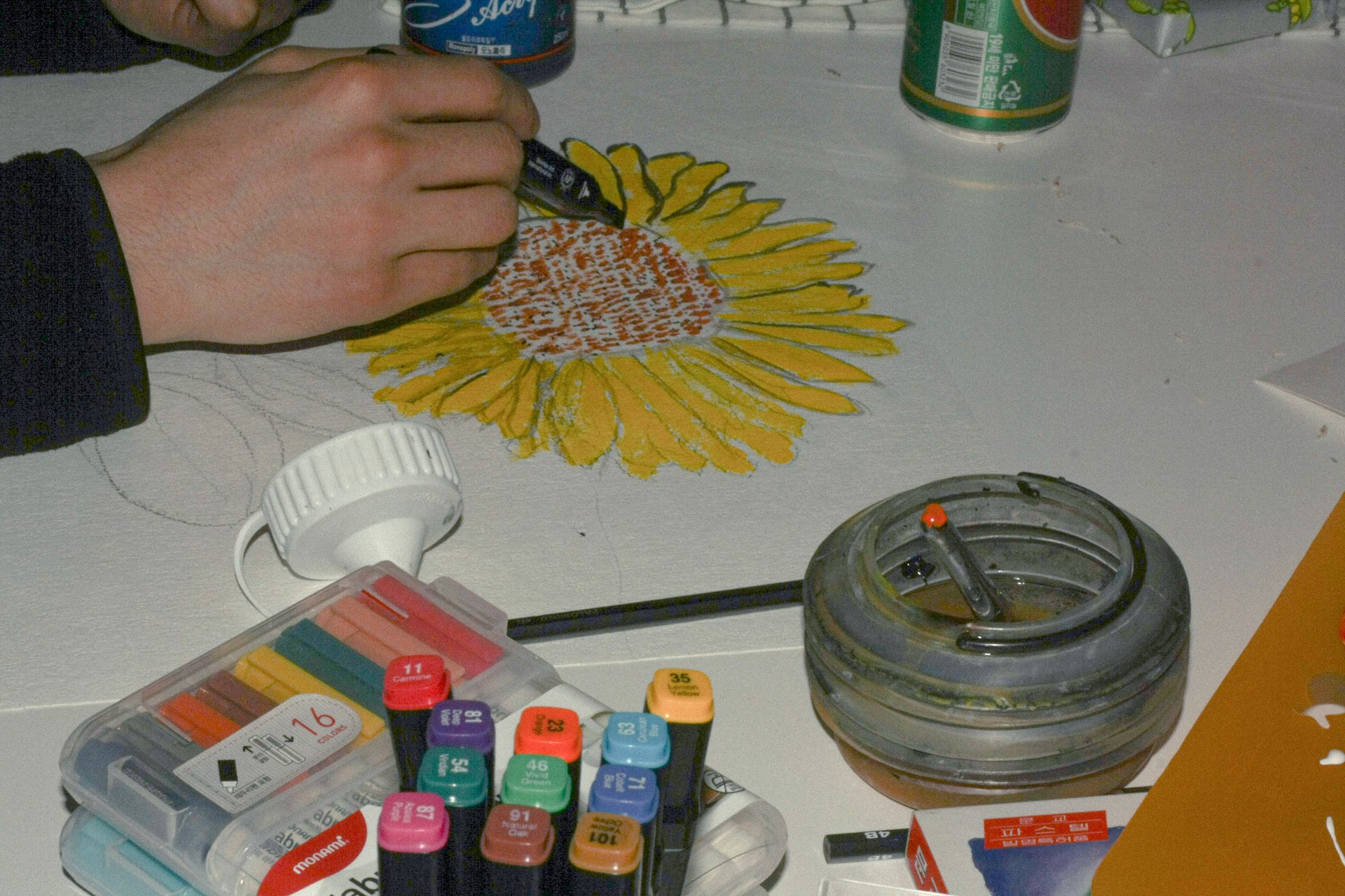 Personne coloriant une fleur jaune sur une table avec des marqueurs, de la peinture.